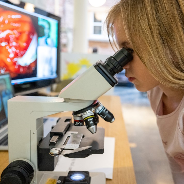 Jonge deelneemster kijkt door microscoop Jonge deelneemster kijkt door microscoop