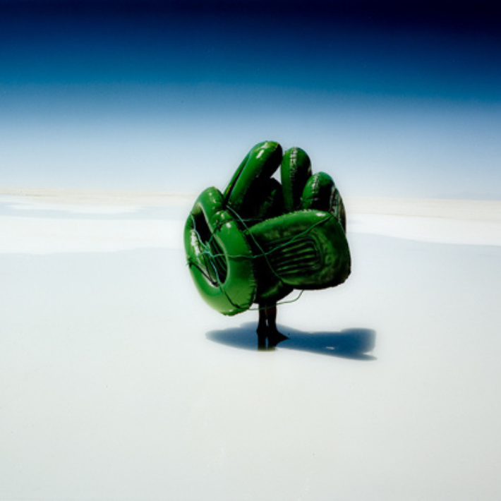 Afbeelding:persoon met groene rubberboten op witte ondergrond en het donkerblauwe/lichtblauwe lucht. 